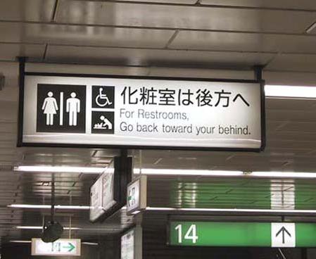 Sign with Japanese on top and below it reads. 'For restrooms, go back towards your behind.'
